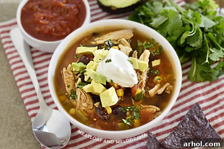 A large white bowl filled with Instant Pot Chicken Taco Soup, generously topped with sour cream and avocado slices, showcasing the rich colors of black beans and corn.
