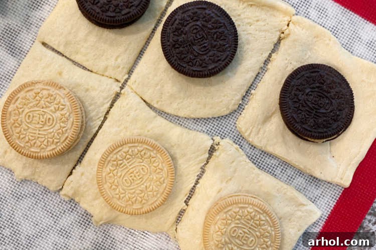 Several Oreo cookies, including classic chocolate and lemon varieties, resting on pre-cut crescent roll sheet dough squares, ready for the wrapping stage.