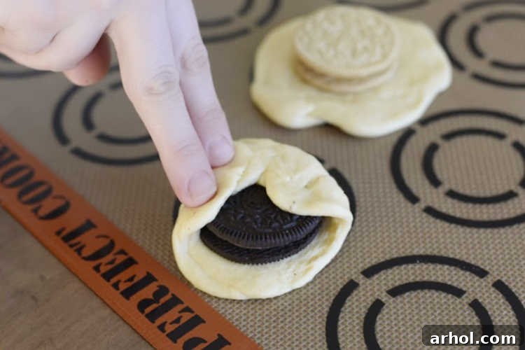 A pair of hands expertly demonstrating the technique of folding crescent dough over an Oreo cookie, carefully pressing and sealing the edges to ensure complete enclosure.