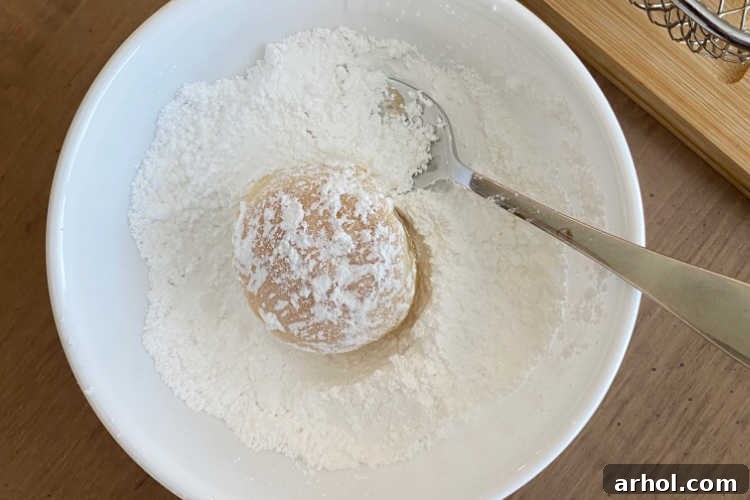 A warm, freshly air-fried Oreo being gently lowered into a bowl of powdered sugar, ensuring a thorough and even coating for that classic finish.