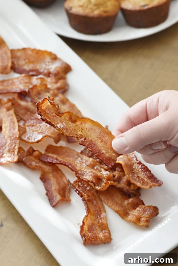 cooked bacon in hand over platter of crispy bacon