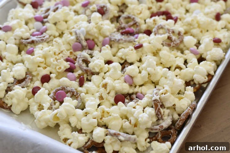 Sweetheart Snack Medley 4 A baking sheet filled with popcorn, pretzels, and white chocolate, adorned with pink and red M&M candies, ready for the next step.