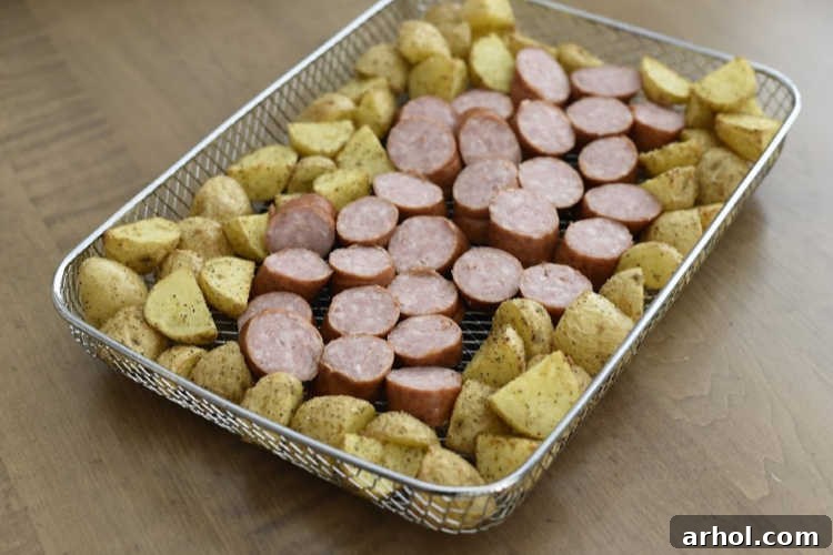 Sliced smoked sausage being added to the air fryer basket alongside par-cooked potatoes for the final cooking stage, ensuring harmonious textures.