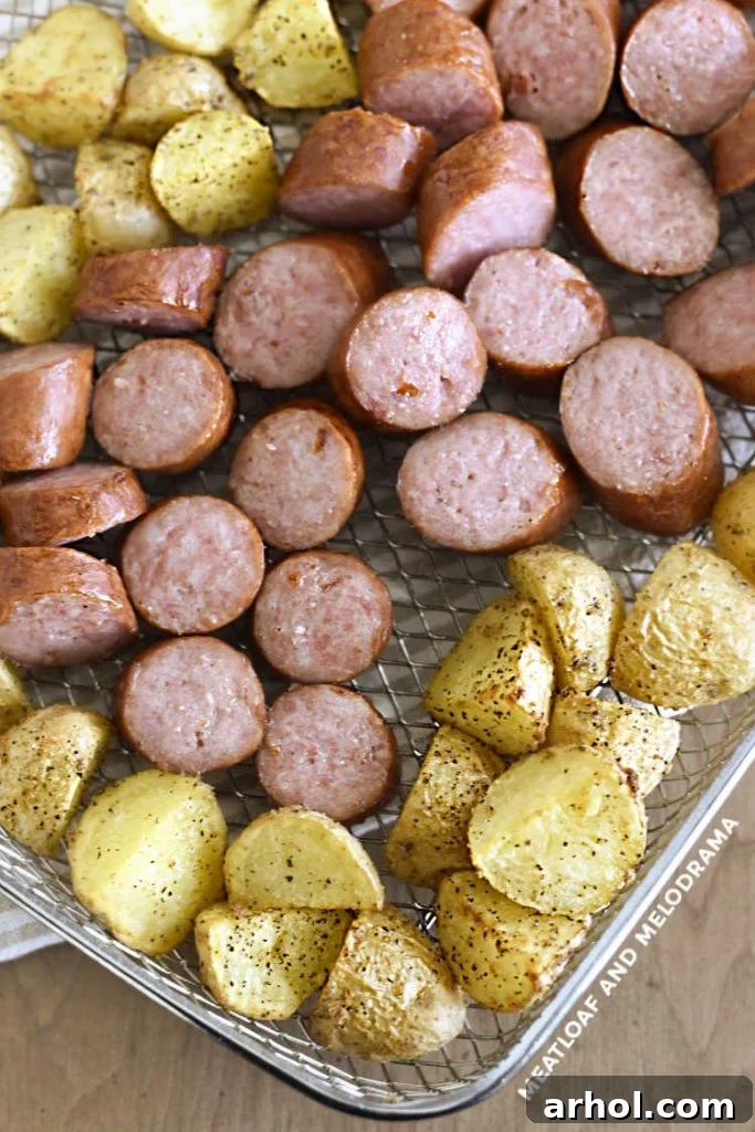 Air-fried kielbasa and potatoes presented in a metal serving tray, indicating a ready-to-eat, wholesome meal, perhaps with a side of green peas.