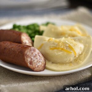 Baked pierogies and kielbasa sausage on white plate with peas