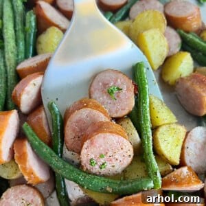 Sheet pan smoked sausage and potatoes with green beans on metal spatula