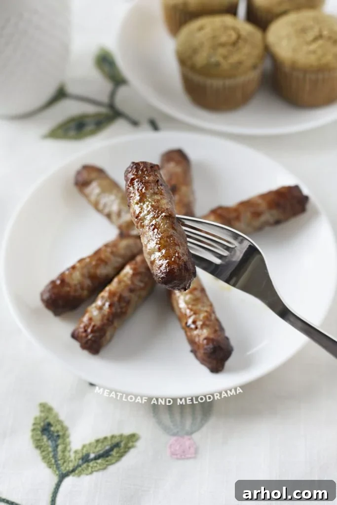 A single, perfectly air-fried breakfast sausage link impaled on a fork, ready for tasting.