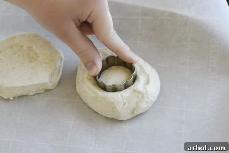 Using a small cookie cutter to carefully cut a hole in the center of a biscuit for making air fryer donuts.