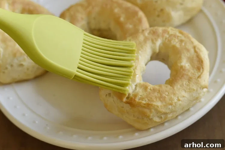 A hand brushing melted butter over a warm air fryer biscuit donut on a white plate, preparing it for cinnamon sugar coating.