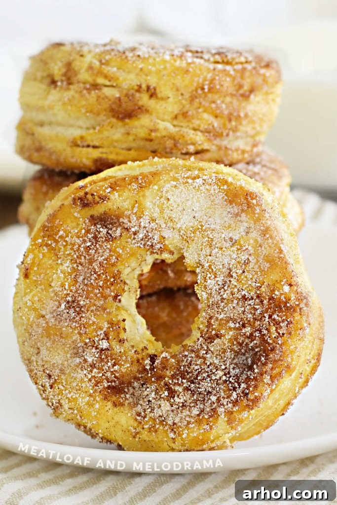 A stack of golden-brown cinnamon sugar air fryer donuts, showcasing their fluffy texture, artfully arranged on a rustic wooden board.