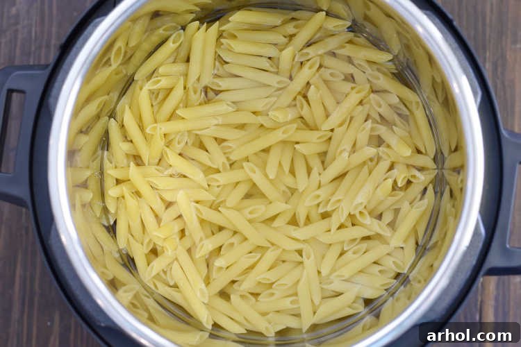 Penne pasta and water are placed inside the Instant Pot inner pot, ready for pressure cooking.