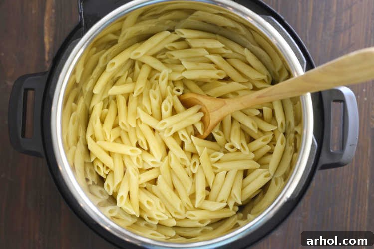A wooden spoon stirring perfectly cooked penne pasta inside an Instant Pot, showing the steam released after cooking.