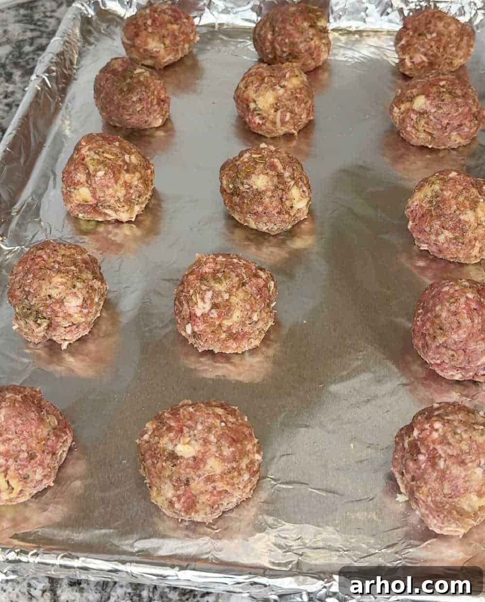 Step 3: Unbaked meatballs neatly arranged in rows on a foil-lined baking tray.