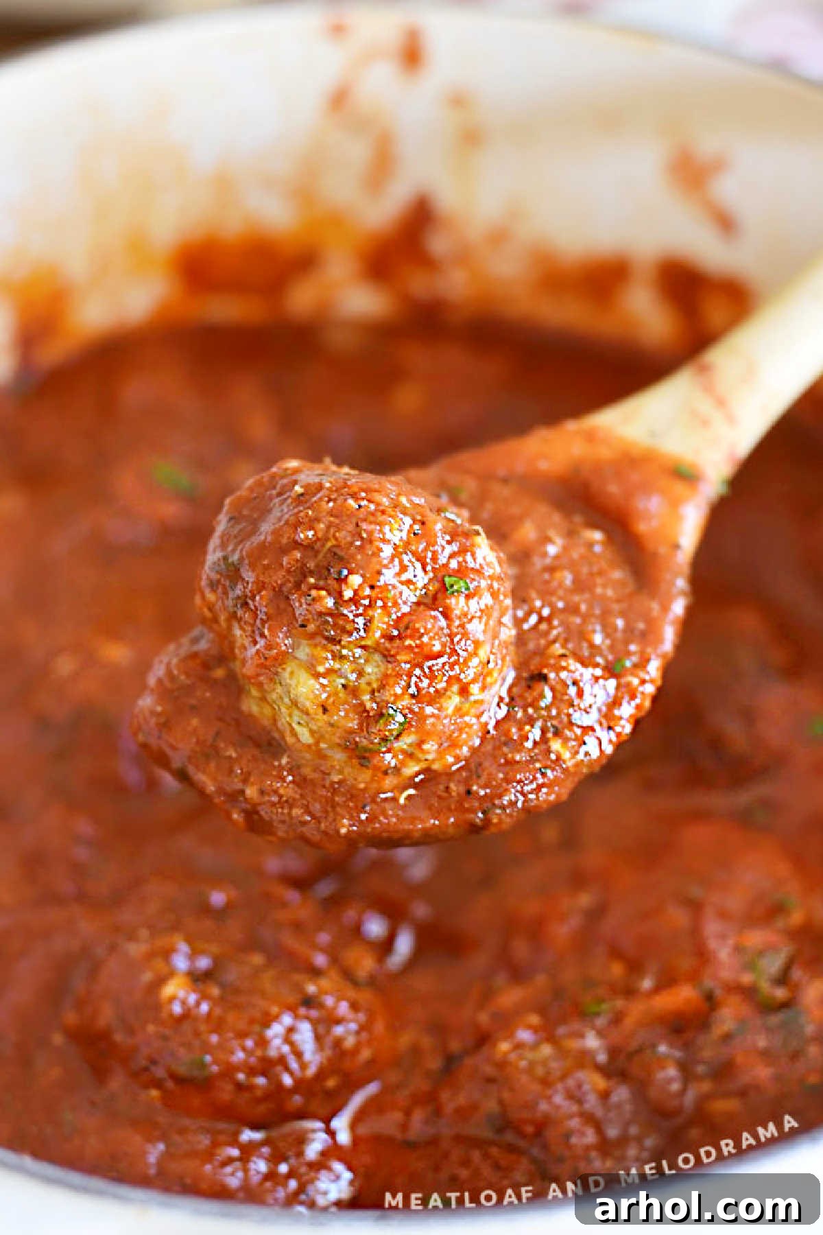 A single baked Italian meatball coated in rich marinara sauce, resting on a wooden spoon, ready to be enjoyed.