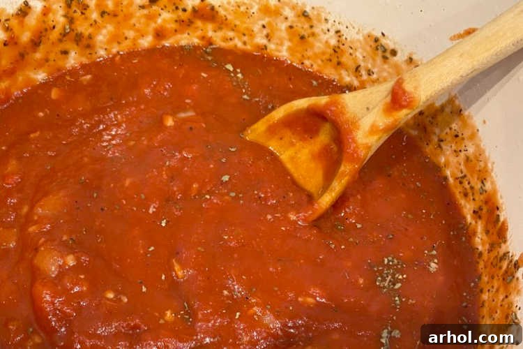 A wooden spoon stirring rich, red homemade tomato sauce in a pot, showcasing its perfect consistency.