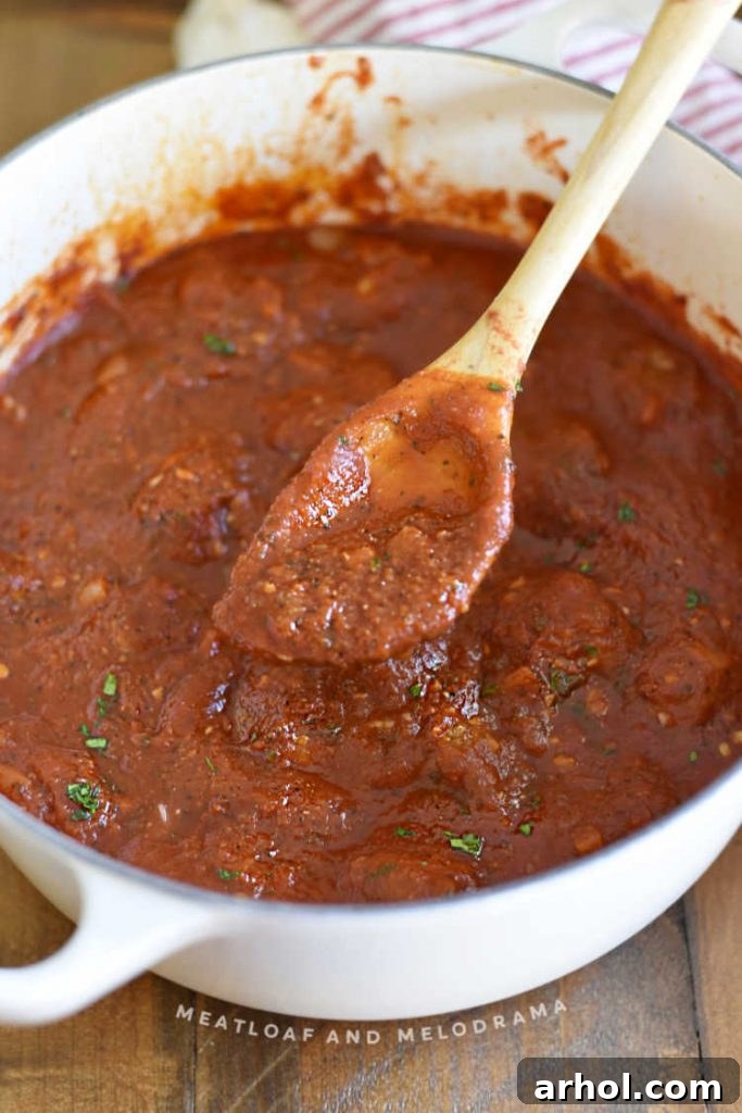 Thick, homemade pasta sauce being stirred with a wooden spoon in a Dutch oven after simmering, ready for serving.