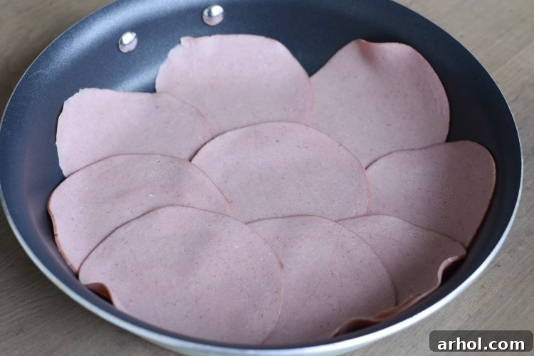 Slices of bologna sizzling in a hot frying pan, edges starting to crisp and curl.