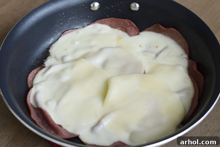 Fried bologna slices covered with melted provolone cheese in a skillet.
