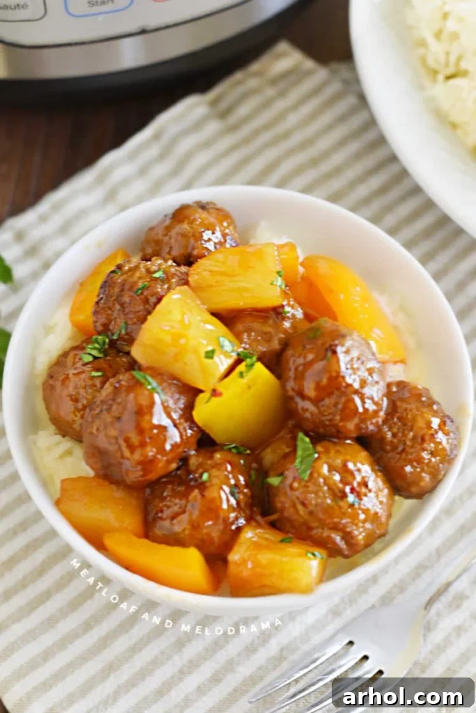Sweet and sour meatballs with pineapple chunks and bell peppers served over jasmine rice in a bowl.
