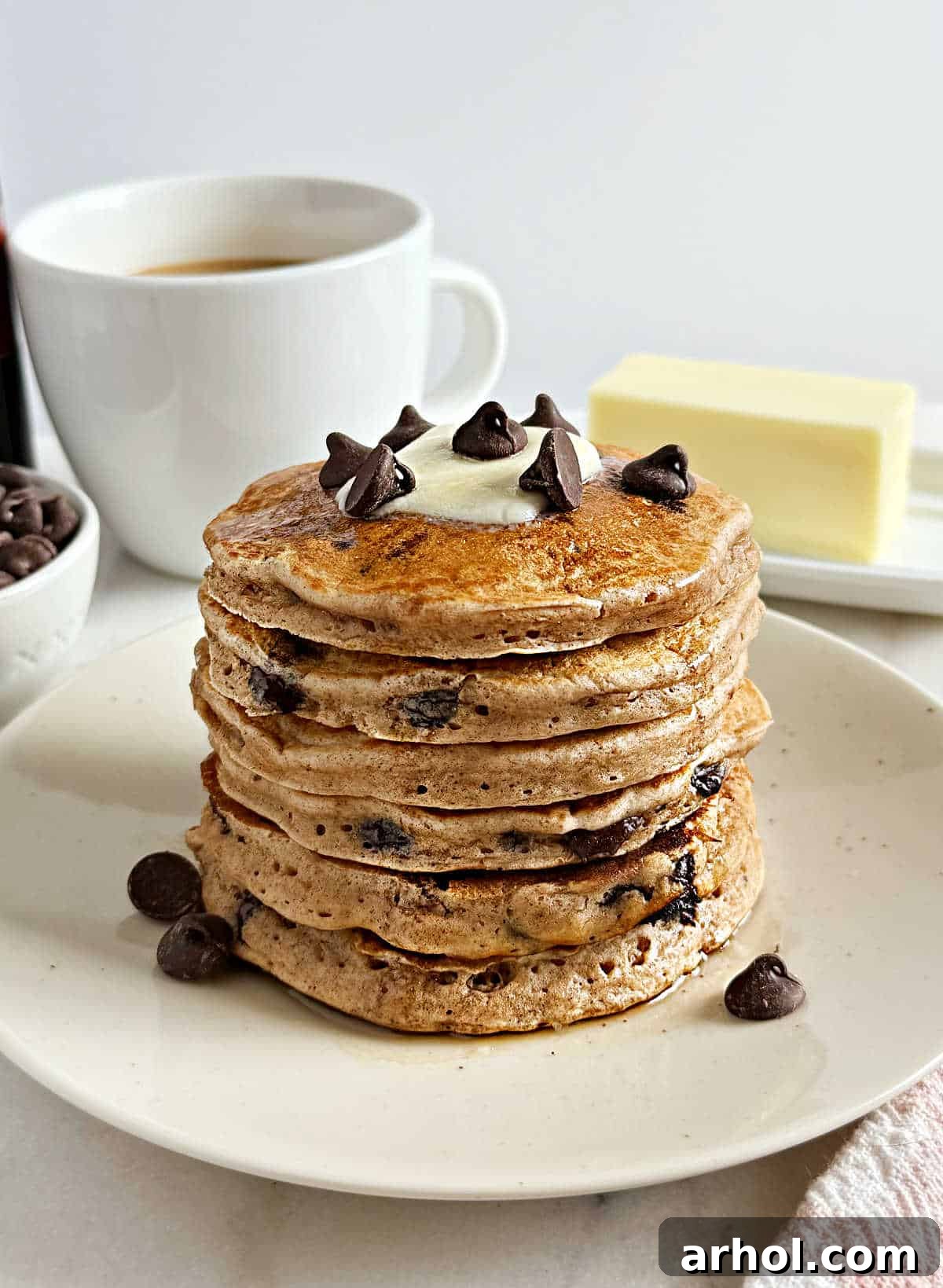 Stacked chocolate chip pancakes with melted butter and chocolate pieces on top, inviting you to indulge in a delicious breakfast.
