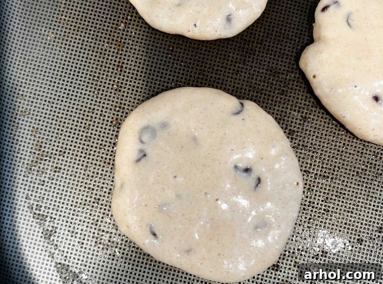 Chocolate chip pancakes cooking on a hot griddle, with visible bubbles indicating they are almost ready to flip.