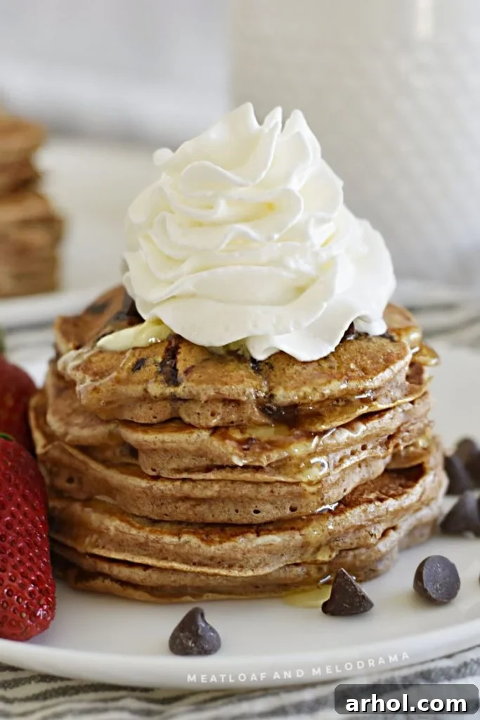 A tall stack of chocolate chip pancakes generously topped with whipped cream and more chocolate morsels, ready to be enjoyed.