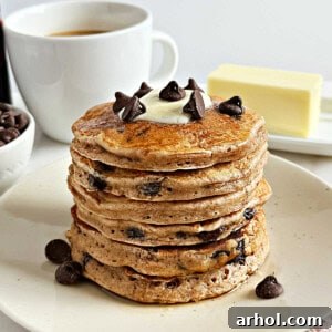 A stack of golden brown chocolate chip pancakes with a pat of butter melting on top, garnished with a few loose chocolate chips.