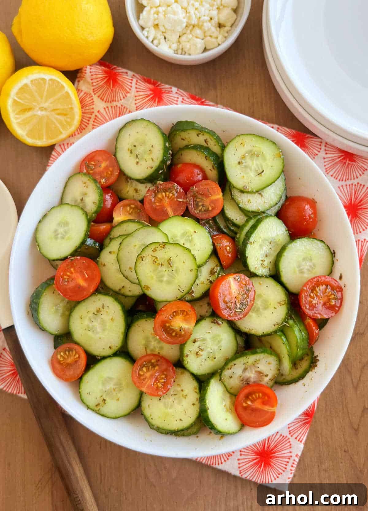 A vibrant cucumber tomato salad with lemon slices and feta cheese in a white serving bowl, ready to be enjoyed on a hot summer day.