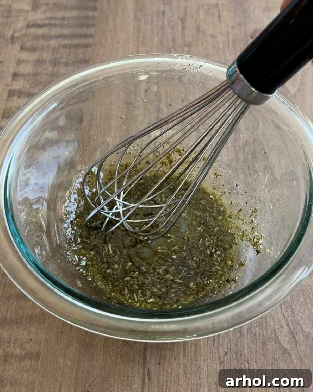 A close-up image showing dressing ingredients being whisked together in a small white bowl, illustrating the first step of the recipe.