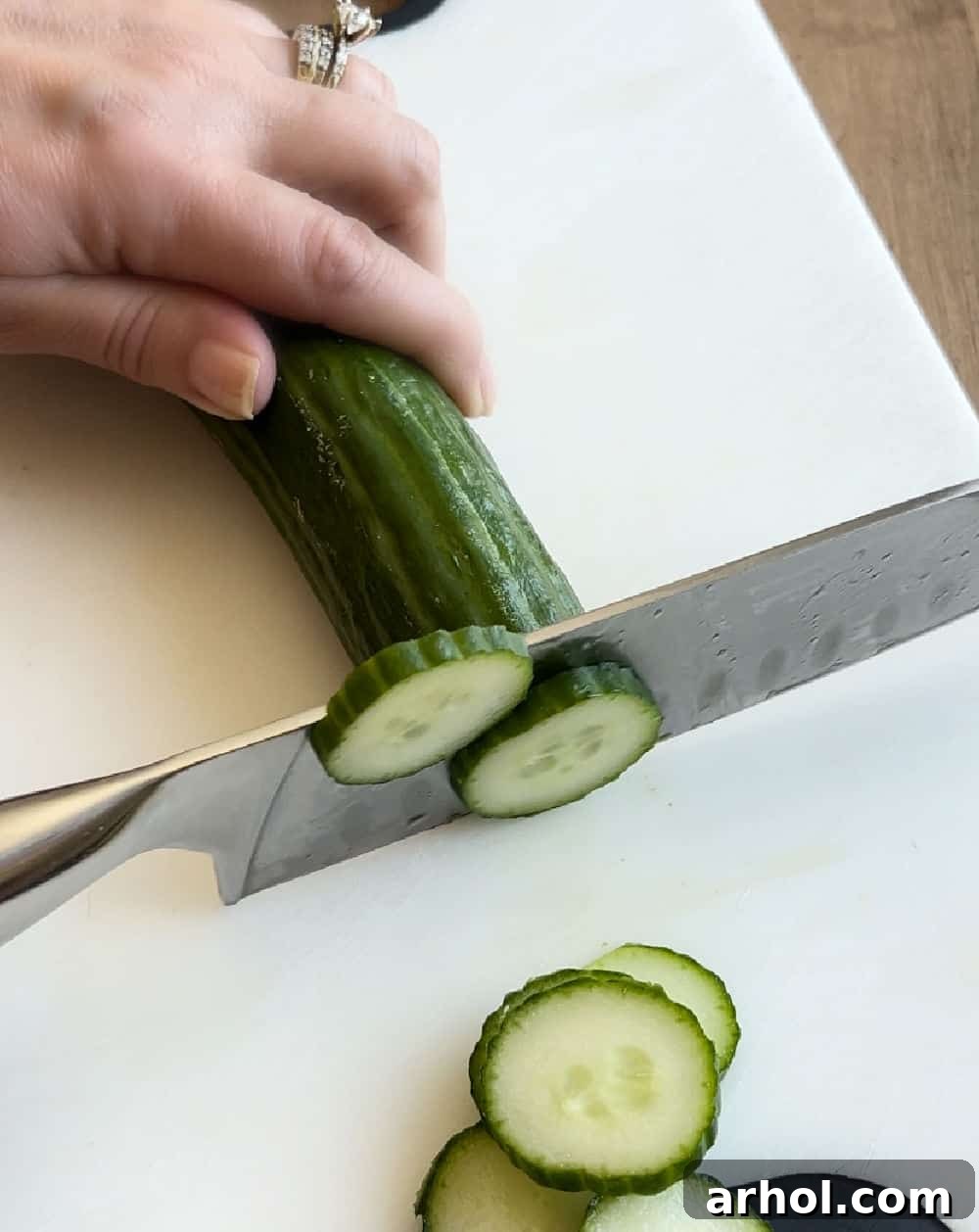 A hand slicing an English cucumber into thin rounds on a cutting board, demonstrating the preparation step for the salad.