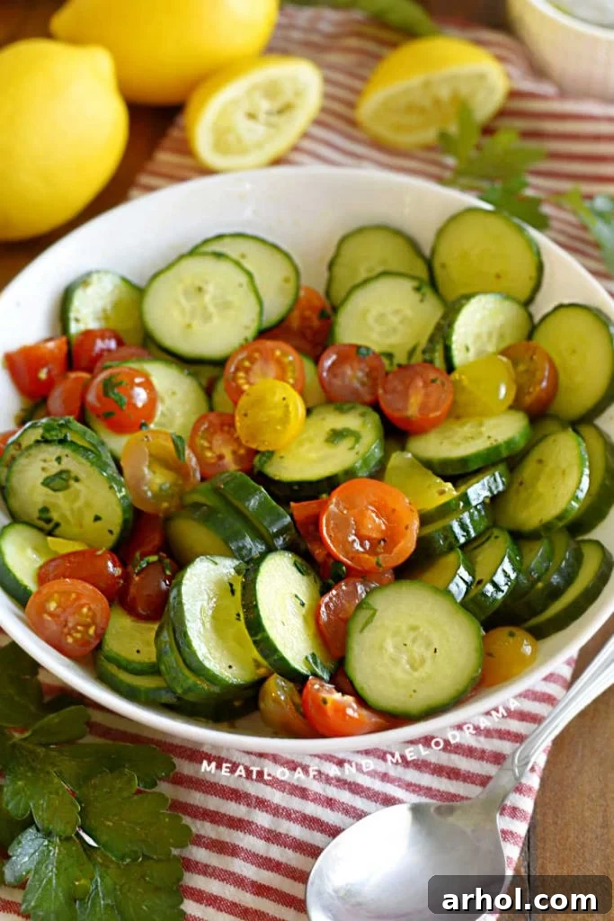 A close-up of sliced cucumbers and grape tomatoes artfully arranged in a white serving bowl, garnished with fresh lemon slices, highlighting the vibrant colors and freshness of the salad.