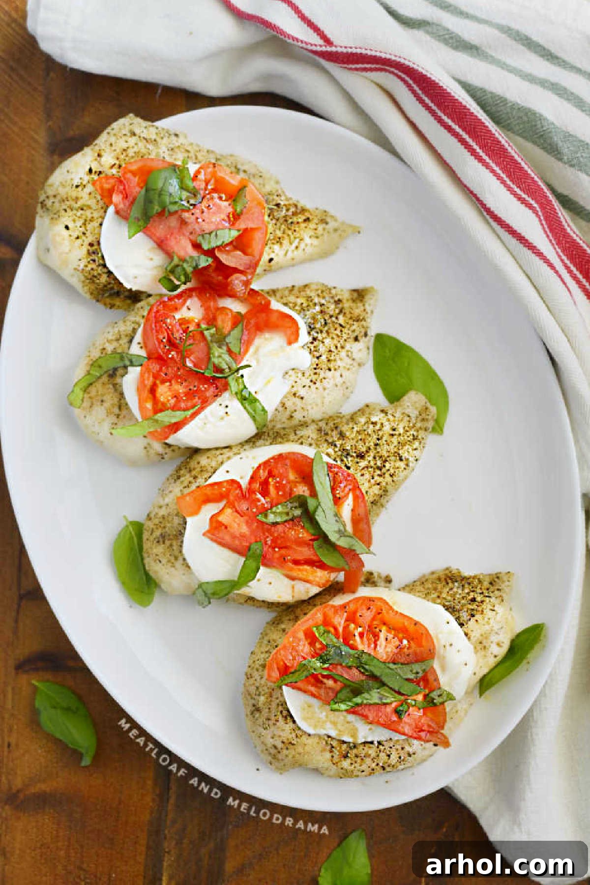 Platter of golden baked Caprese chicken breasts topped with melted mozzarella, bright red tomato slices, and fresh green basil leaves, ready to serve.