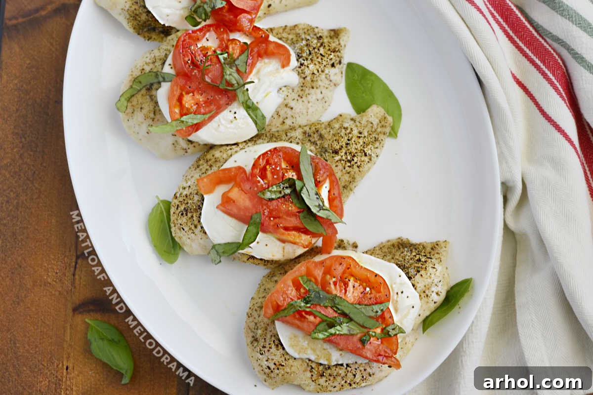 Close-up of a caprese chicken breast on a platter, showcasing the melted mozzarella, bright red tomato slices, and fresh green basil leaves.