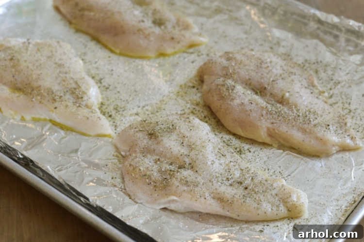 Seasoned, uncooked boneless, skinless chicken breasts arranged neatly on a sheet pan, ready for baking.