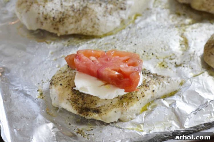 Baked chicken breasts topped with melting fresh mozzarella and bright red tomato slices on a sheet pan, just removed from the oven.