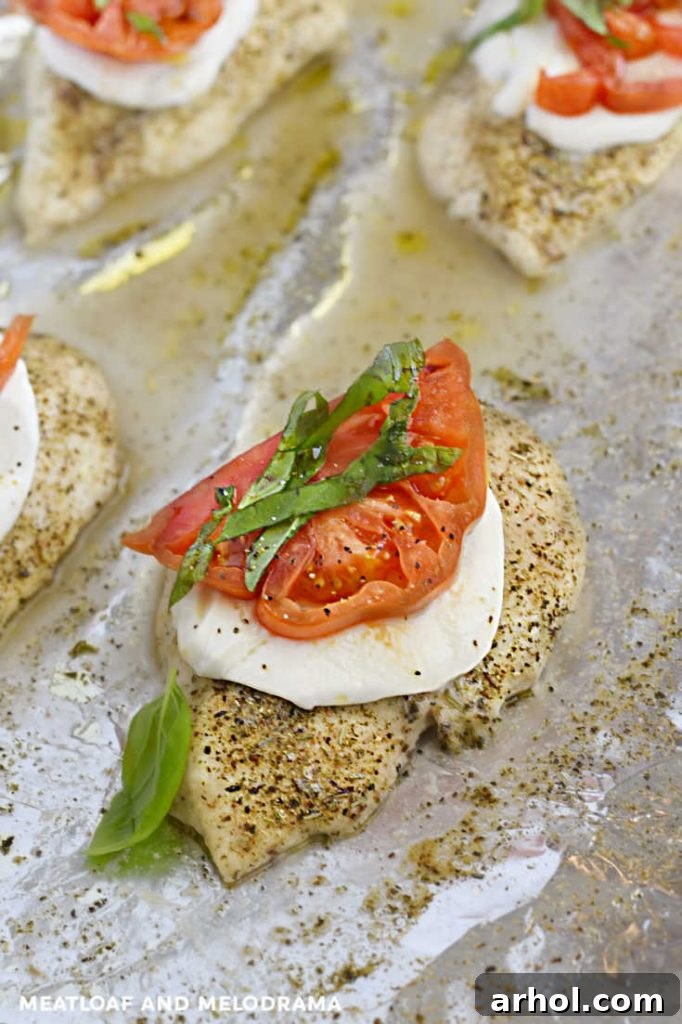 Finished baked Caprese chicken breasts with melted mozzarella, tomato, and fresh basil, artfully arranged on a sheet pan.