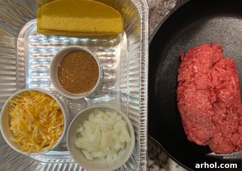 A vibrant selection of ingredients for oven baked tacos, including lean ground beef, taco seasoning packet, a block of cheddar cheese, red onion, and hard taco shells.