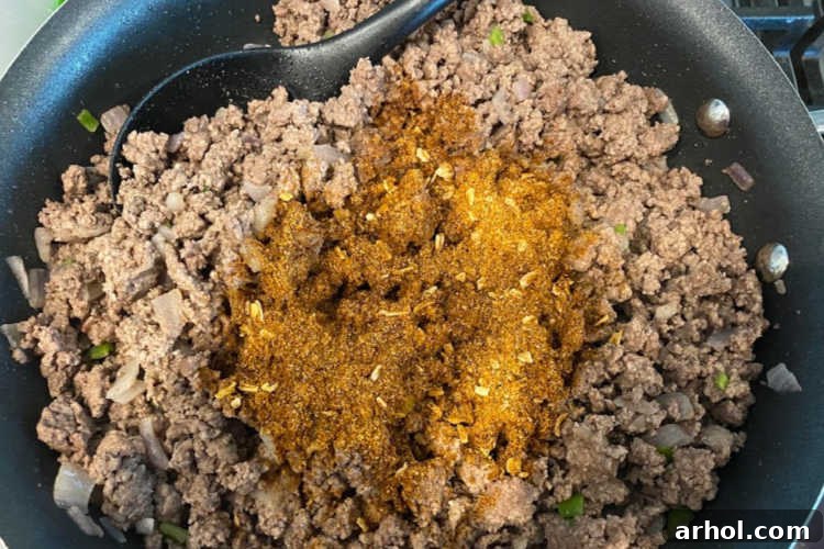 Adding taco seasoning to browned ground beef in a large skillet, ready for simmering and infusing with flavor