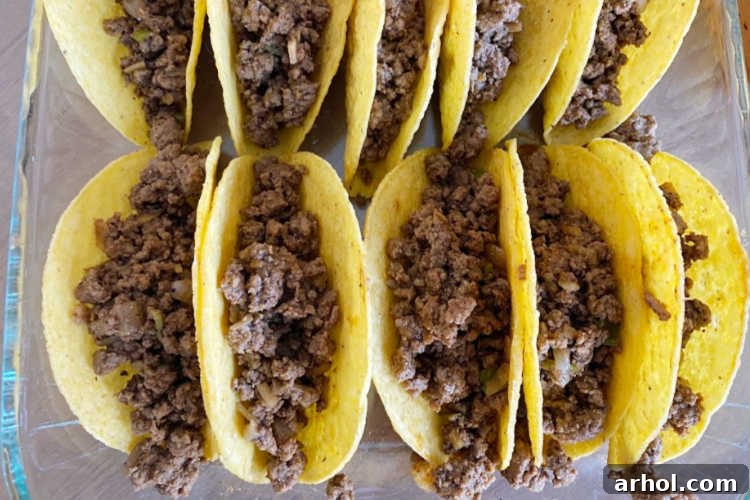 Seasoned ground beef filling scooped into hard corn taco shells, arranged neatly in a baking dish