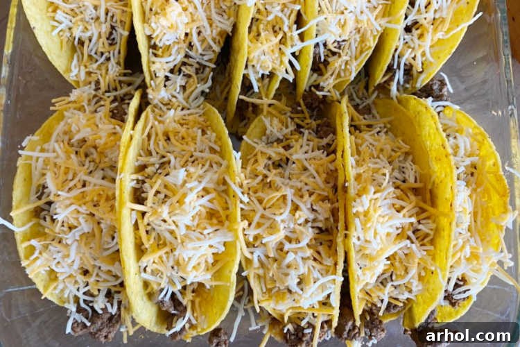 A close-up shot of shredded cheese liberally sprinkled over seasoned ground beef filling in taco shells, ready for baking