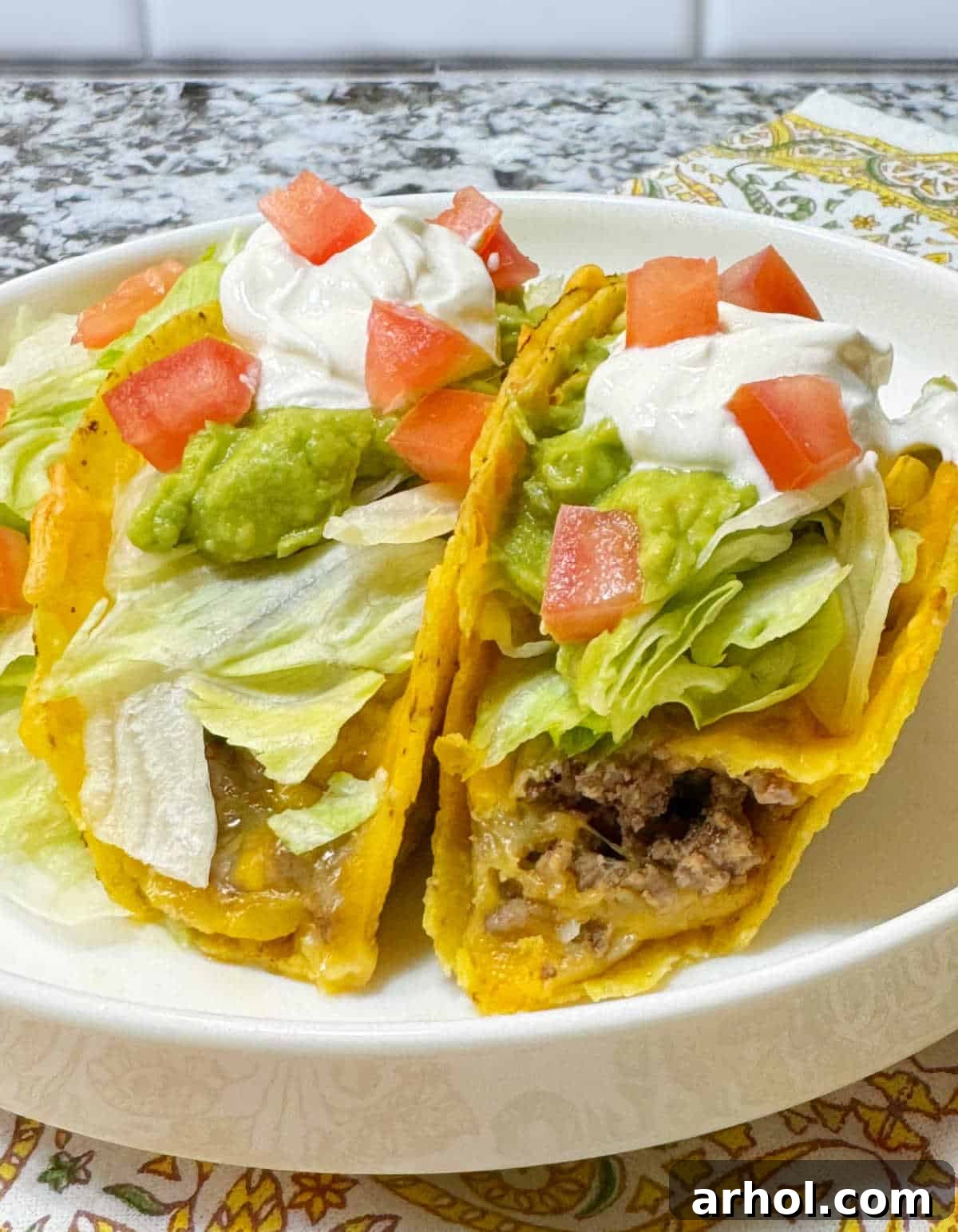 Two perfectly baked tacos with seasoned ground beef, melted cheese, and fresh taco toppings on a serving dish, ready to eat