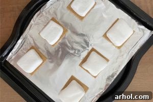 Graham cracker halves with marshmallows on top on baking sheet, ready for baking.