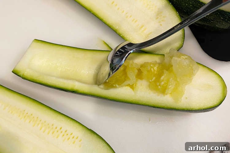 Scooping out the interior of a zucchini half with a teaspoon to create a boat shape.
