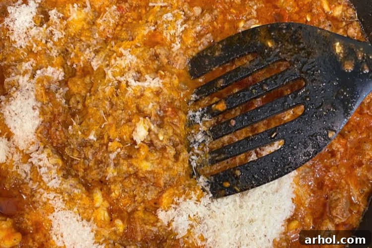 Sausage and onion mixture simmering in marinara sauce with Parmesan cheese in a skillet.