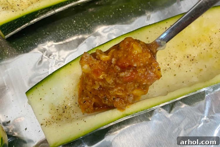 Spoon filling into zucchini halves arranged on a baking sheet.