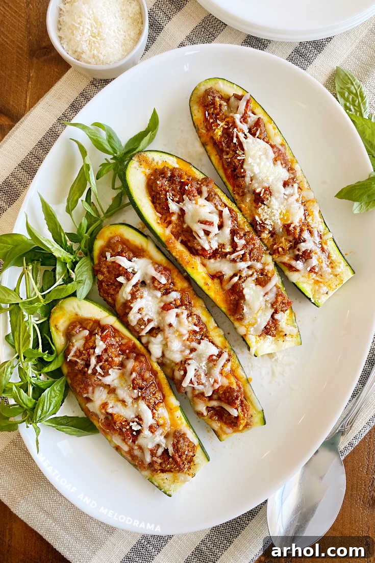 Baked zucchini boats with melted cheese on a white serving platter, garnished with fresh herbs.