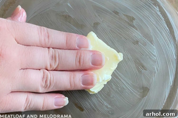 hand spreading butter on a glass pie pan