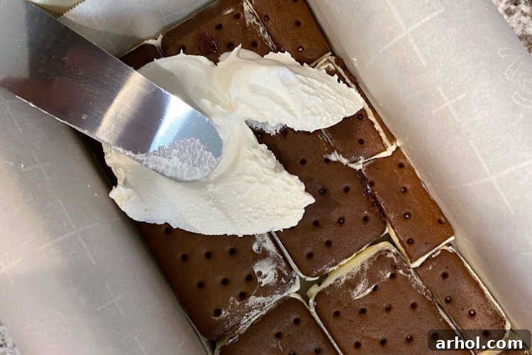 Effortless Ice Cream Sandwich Cake 5 Spreading a smooth layer of whipped topping over the first layer of ice cream sandwiches in the loaf pan.