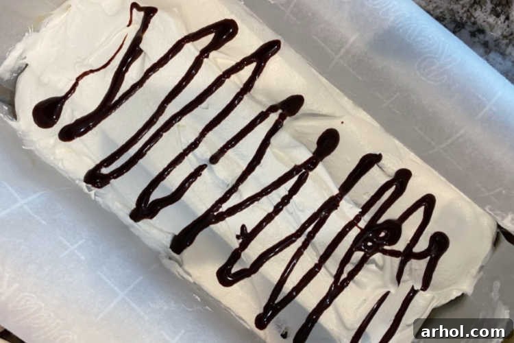 Effortless Ice Cream Sandwich Cake 6 Chocolate syrup being drizzled over the whipped topping layer of the ice cream sandwich cake.