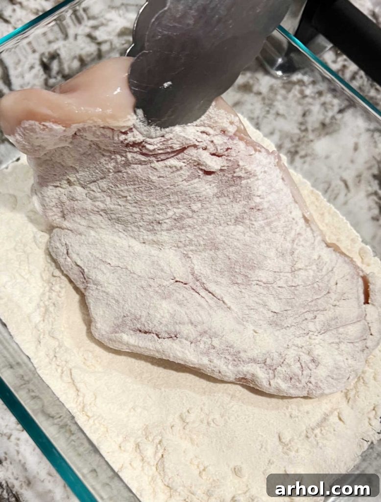 Dredging a chicken cutlet in flour in a shallow dish, preparing it for pan-frying.